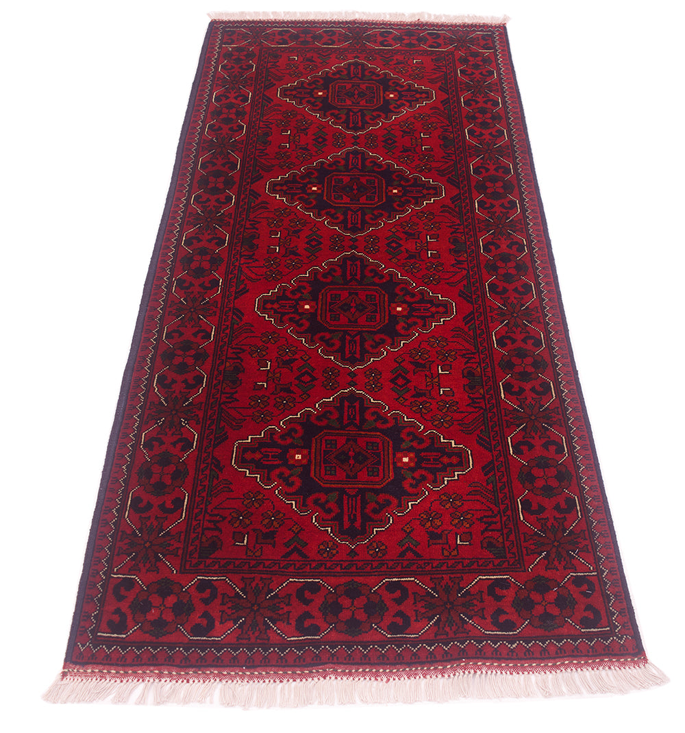 A traditional afghan runner rug with a deep red field, dark navy blue geometric medallions, and cream-colored fringe on the ends.