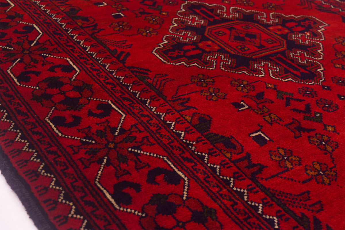 A close-up of a red afghan runner rug with dark navy and beige geometric borders and floral motifs.