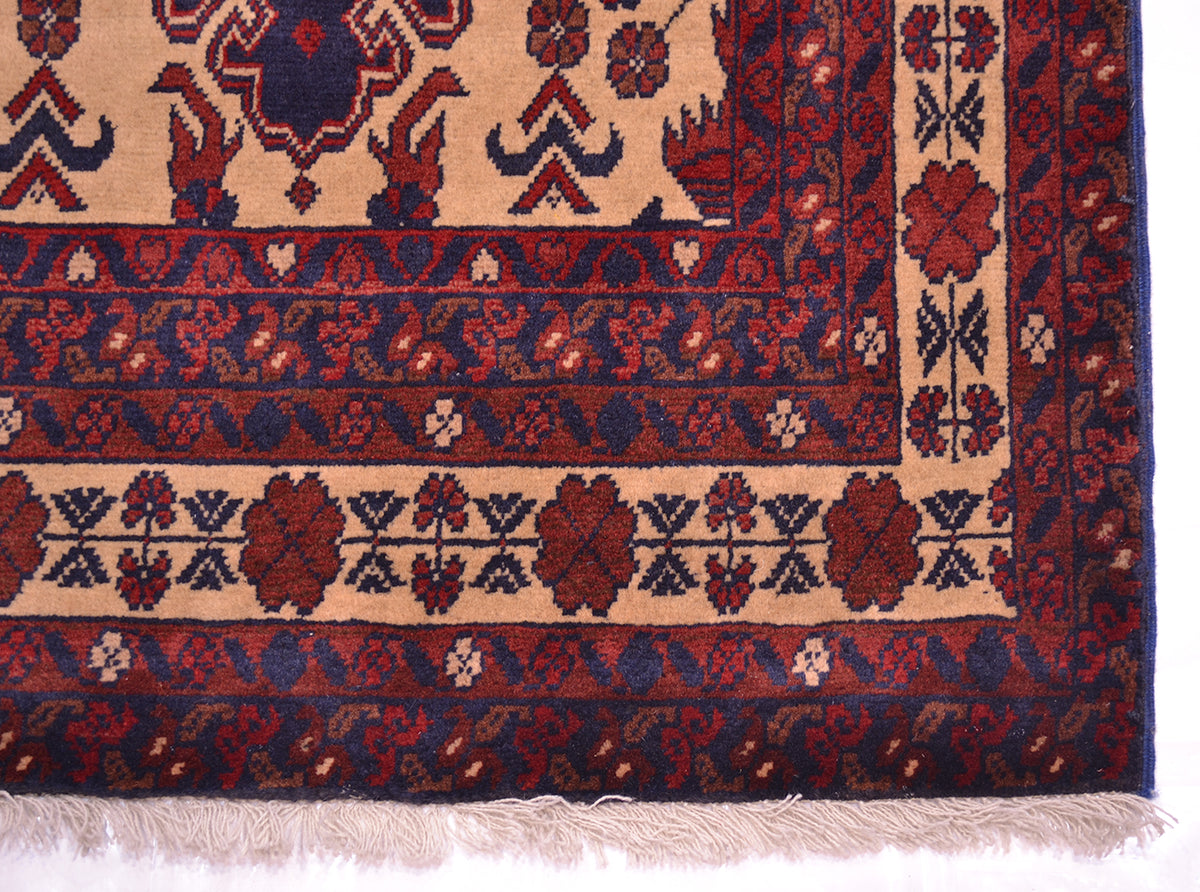A close-up of a traditional runner rug corner showing a beige field with red and navy floral motifs and a red border with cream fringe.