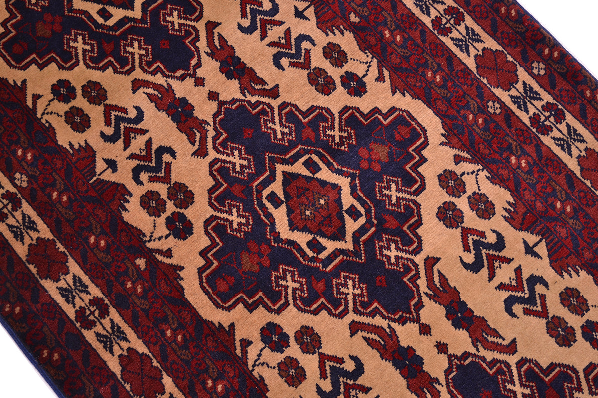 A close-up of a traditional patterned runner/rug with a beige field, dark navy blue medallion, and red border with floral motifs.