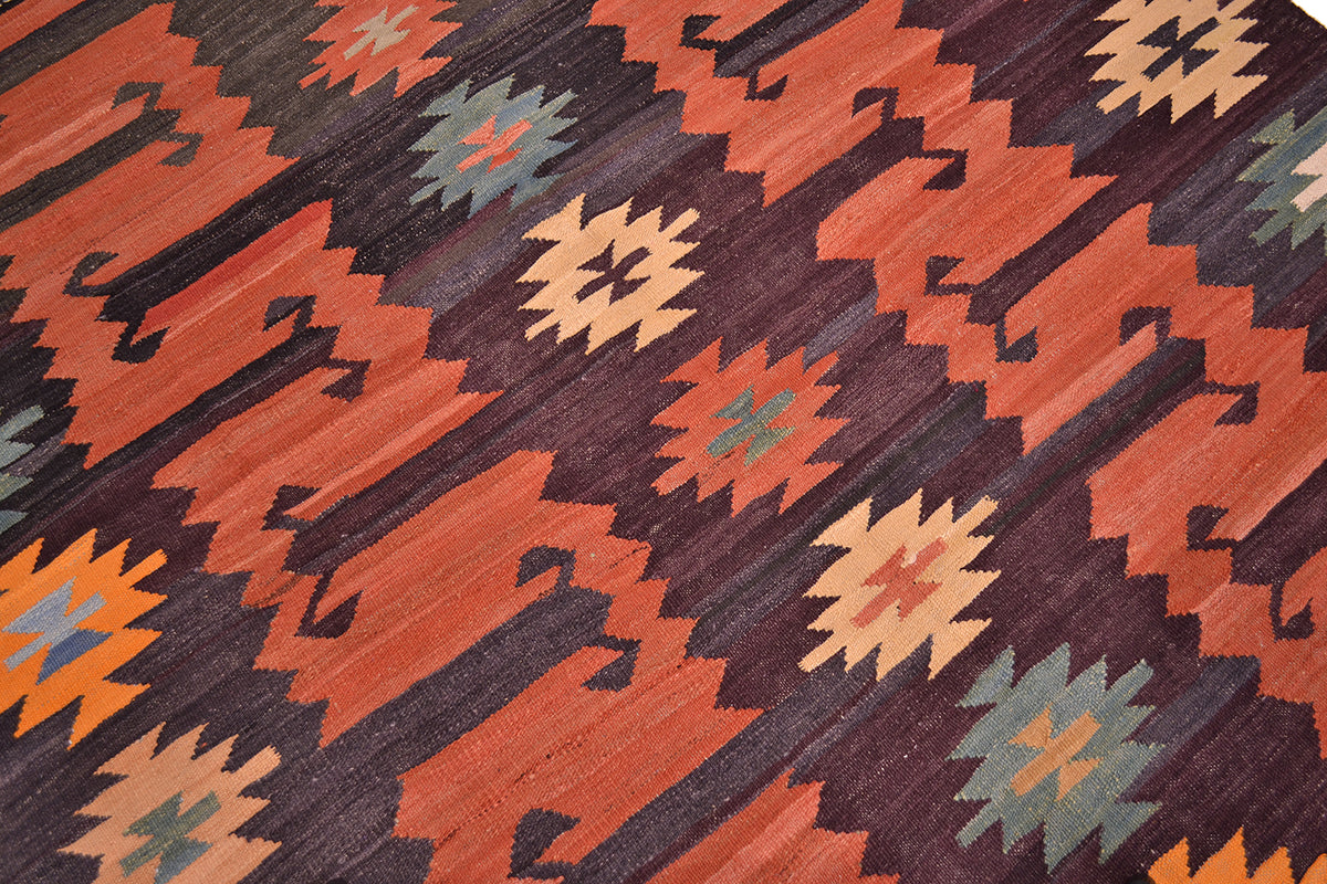 A close-up of a handwoven Afghan Labijar kilim rug with a repeating geometric pattern in terracotta orange, dark brown, beige, muted green, and orange.