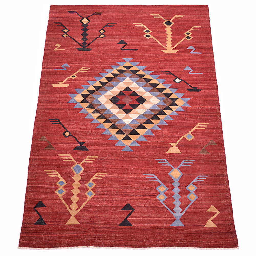 A rectangular handwoven red Labijar Kilim rug with a Southwestern geometric pattern, featuring a large central diamond and stylised tree motifs in beige, blue, black, and red.