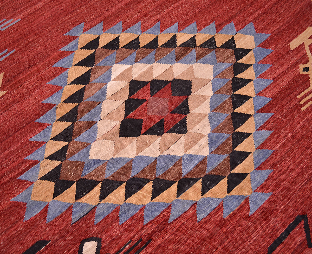 A close-up of a woven Afghan Kilim 3x2m rug featuring a geometric diamond pattern with concentric squares of beige, brown, black, and red, bordered by blue-grey triangles on a red background.