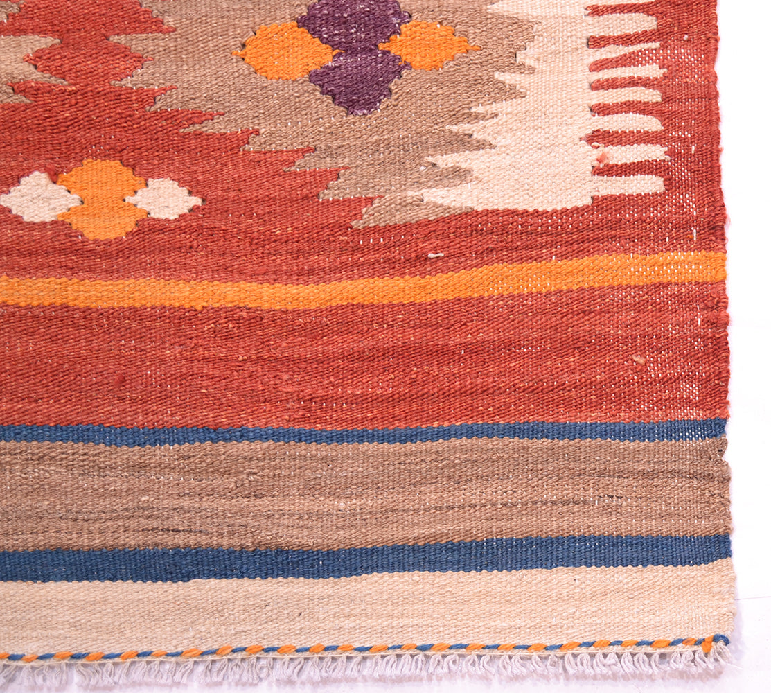 Close-up of a handwoven Labijar Kilim runner corner showing a rust red field, geometric motifs in orange, cream, and purple, horizontal bands of blue and beige, and white fringe.