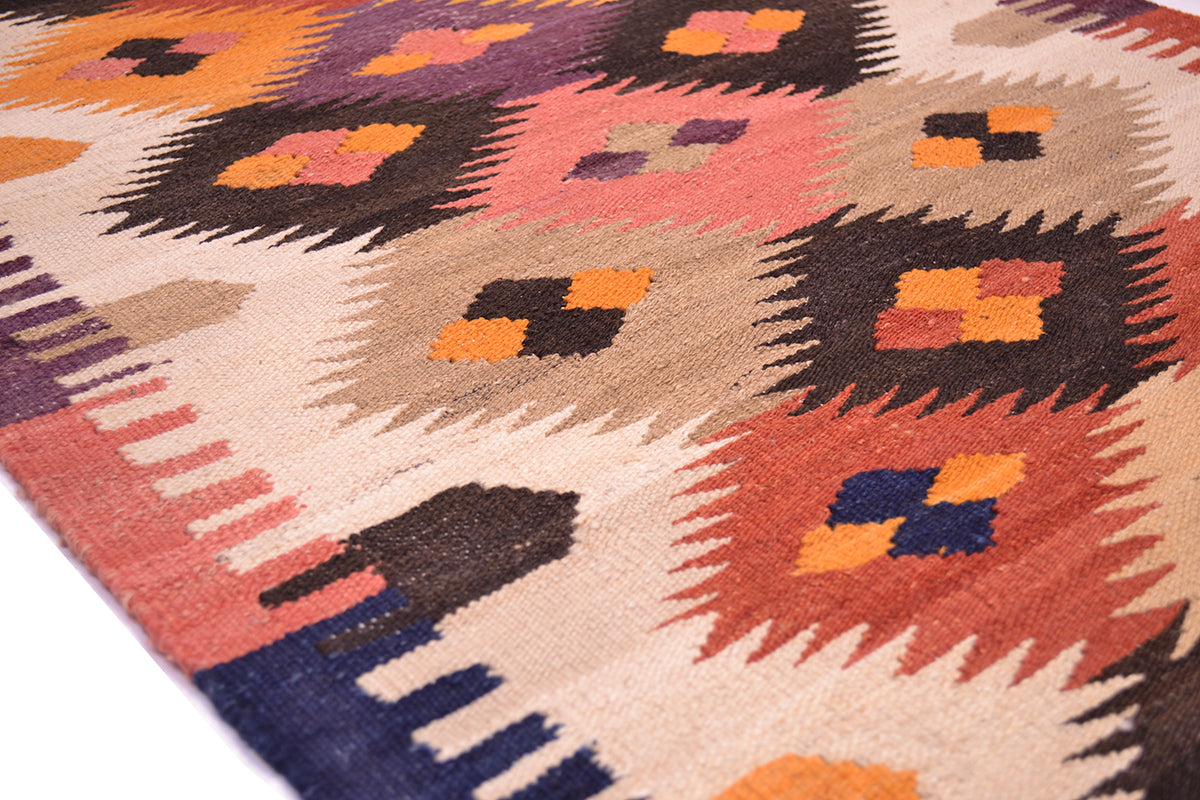 A close-up of a handmade woven Afghan kilim runner with a geometric pattern in orange, pink, brown, beige, and navy blue.
