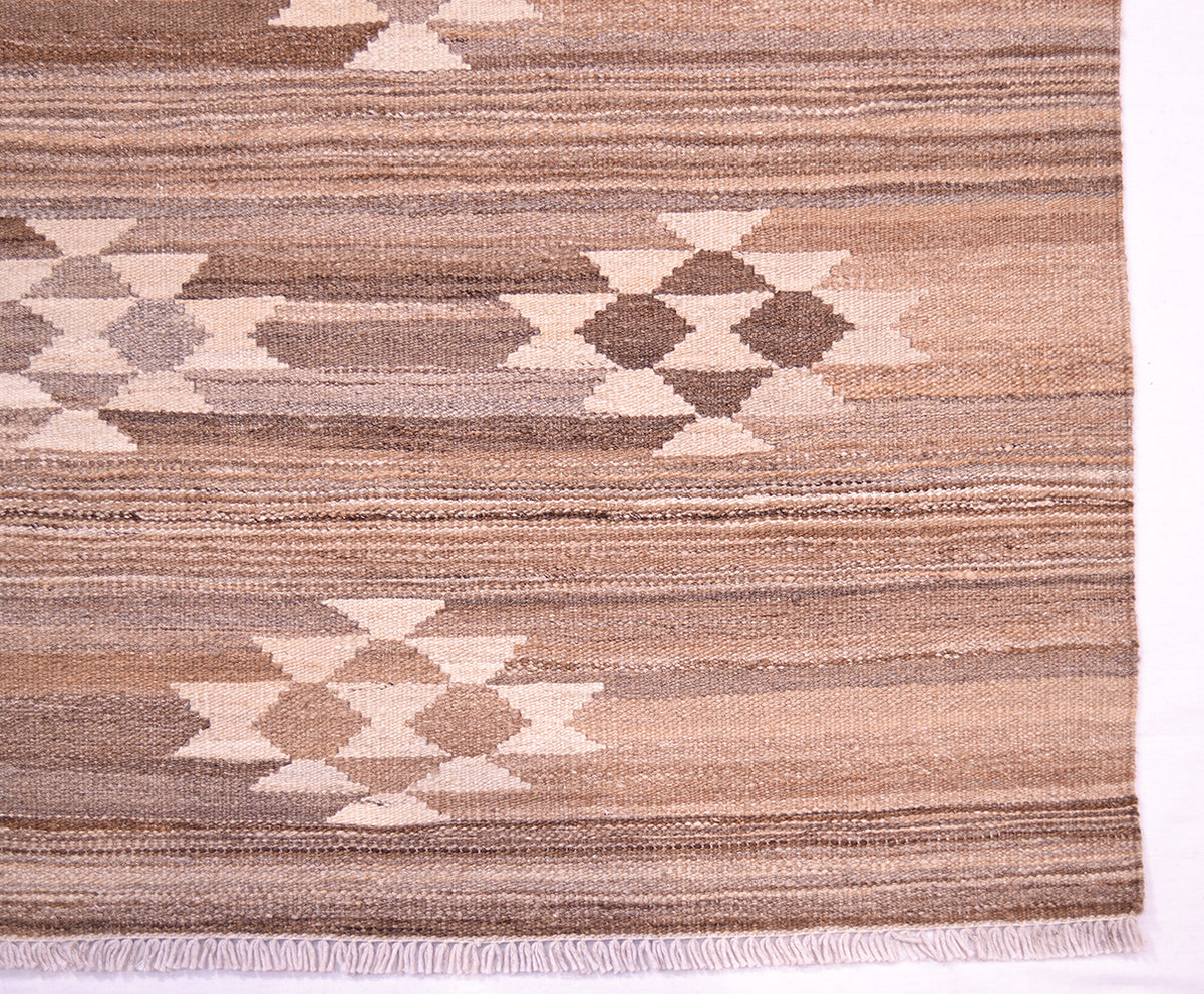 A close-up of a handwoven natural Labijar Kilim with horizontal stripes in beige, taupe, brown, and cream, featuring geometric diamond and star motifs and a short fringe along the bottom edge.