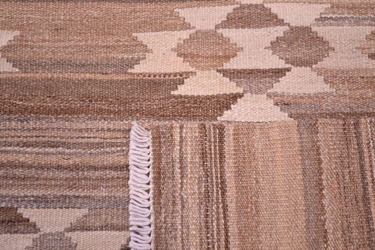 Close-up of the weave of a handwoven Afghan Kilim rug with a geometric pattern in shades of brown, beige, and cream, featuring a white fringed edge.