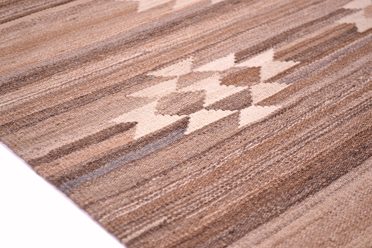 A close-up of a woven Labijar Kilim rug with a geometric pattern in shades of brown, tan, and beige, shown on a white surface.