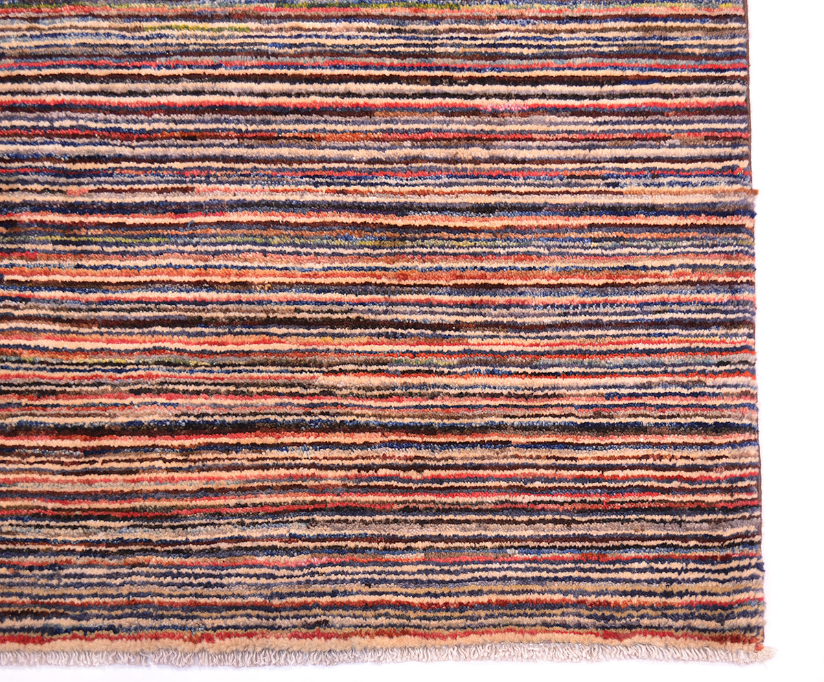 A close-up of a striped handmade Gabbeh rug with horizontal bands in rust orange, navy blue, charcoal grey, beige, and muted pink, finished with a fringed edge on a white background.