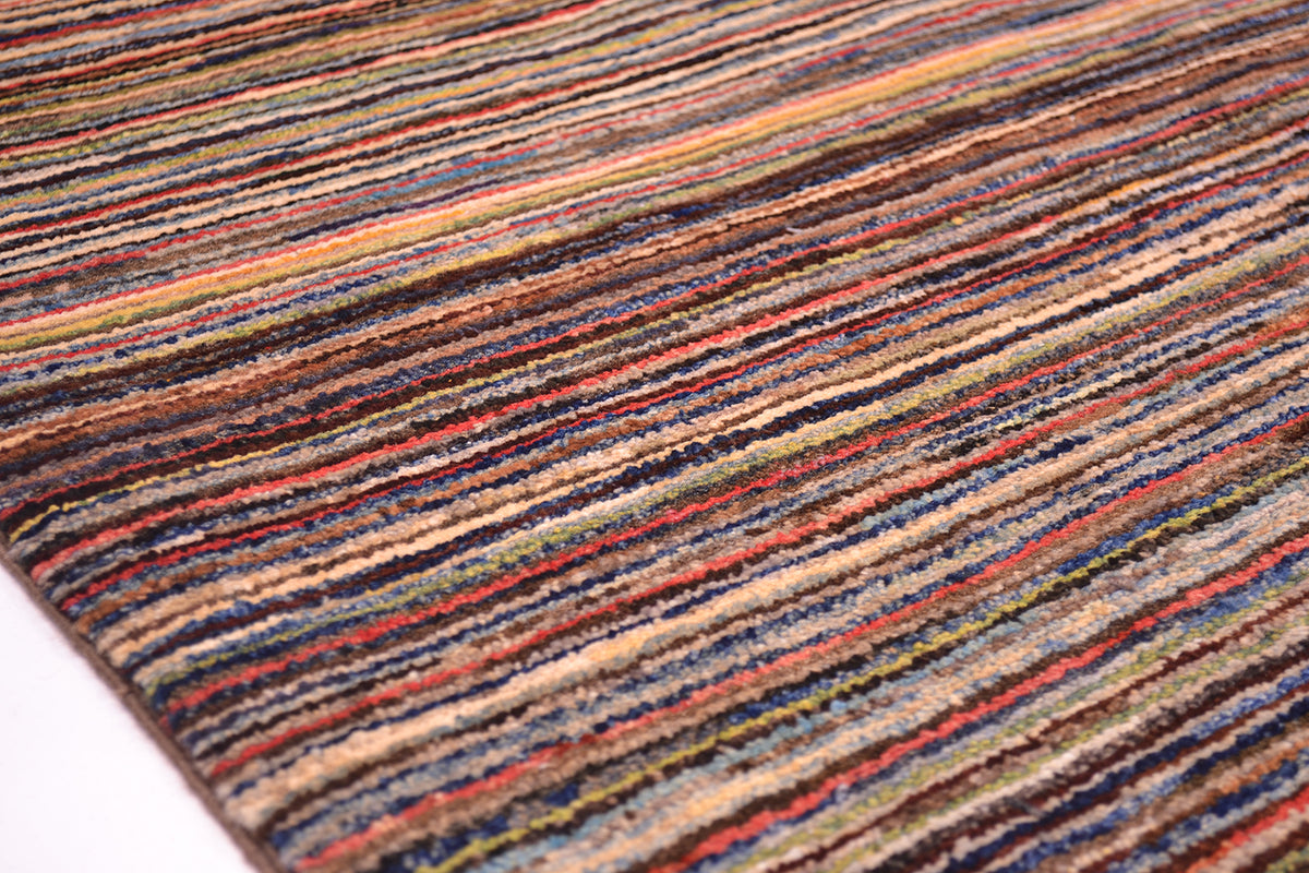 Close-up of a handmade multicolour striped Gabbeh rug with horizontal bands of red, blue, beige, brown, and yellow on a white background.