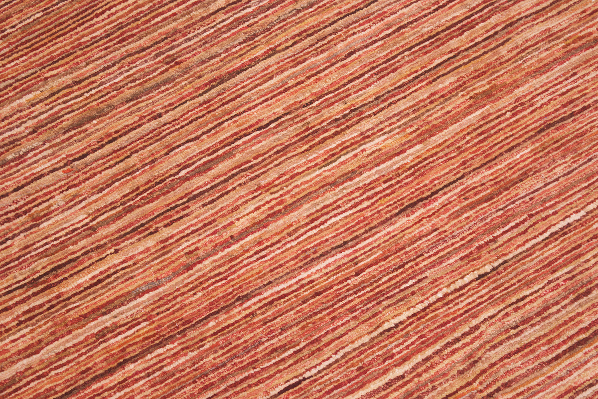 A close-up texture shot of a handwoven Afghan Gabbeh carpet featuring stripes in warm rust red, terracotta, and brown tones.
