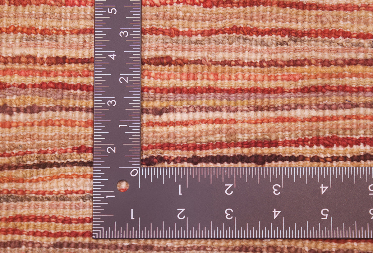 Close-up of the hand-knotted weave of a striped Afghan Gabbeh carpet in warm earthy tones, shown with a dark metal L-shaped ruler to indicate scale of the knotting.