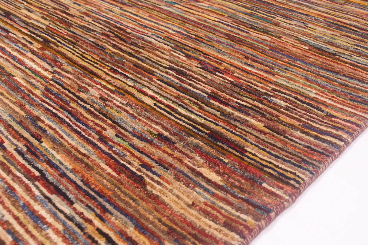 A close-up of a textured Handmade modern Afghan Gabbeh carpet with a multicolour linear stripe pattern in shades of rust, brown, beige, and blue, shown on a white surface.