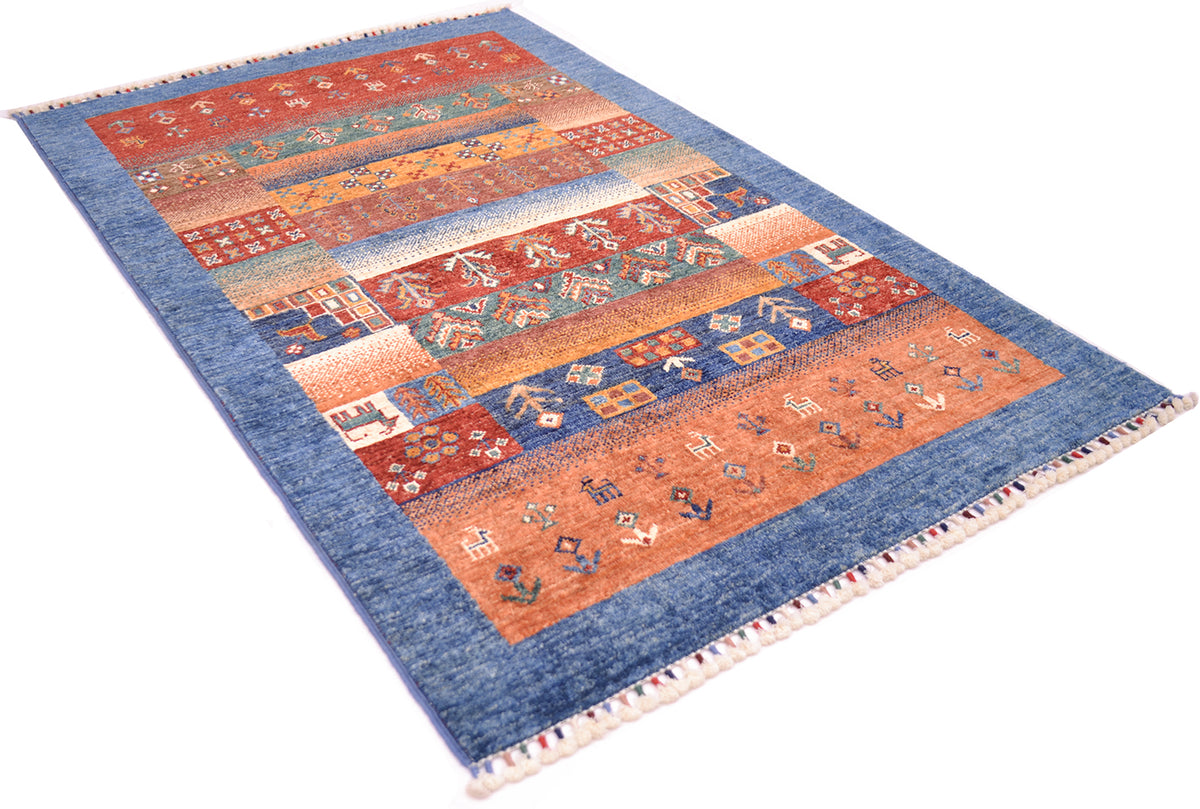 A rectangular Afghan Loribft rug with blue border and a central patchwork design in rust orange, red, beige, and blue, shown on a plain white background.