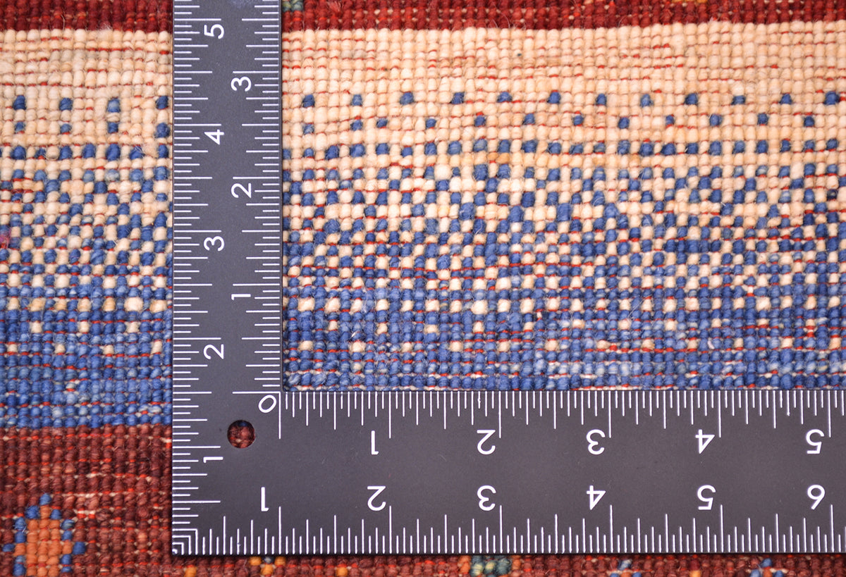 Close-up of a hand-knotted Afghan Loribaft rug showing a geometric pattern in beige, blue, and rust red, with a black L-square ruler placed along the corner to indicate scale of the rug's knotting.