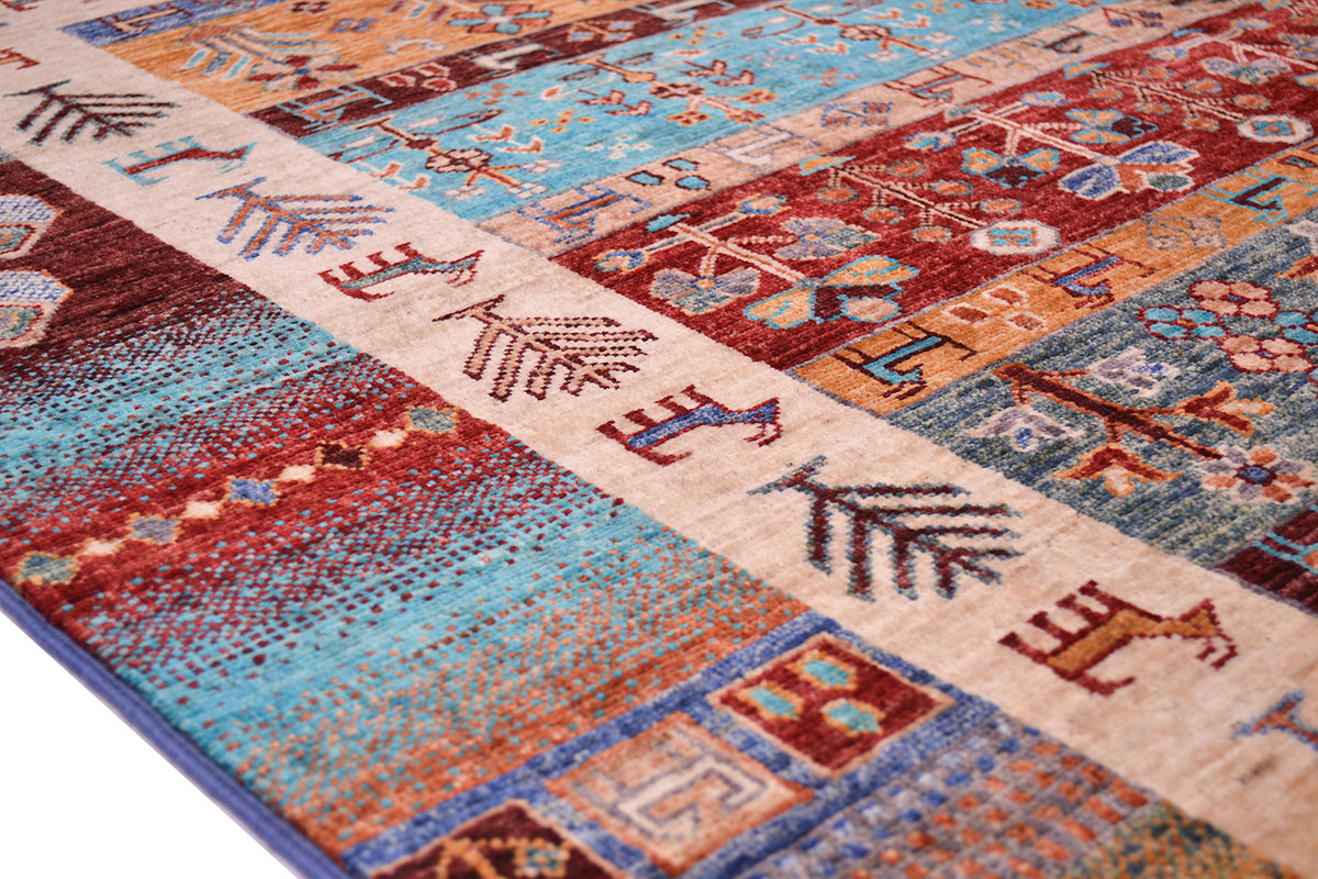 A close-up of a patterned multicolour Loribaft rug with a cream central band and geometric, floral, and animal motifs in turquoise, rust red, blue, orange, and brown.