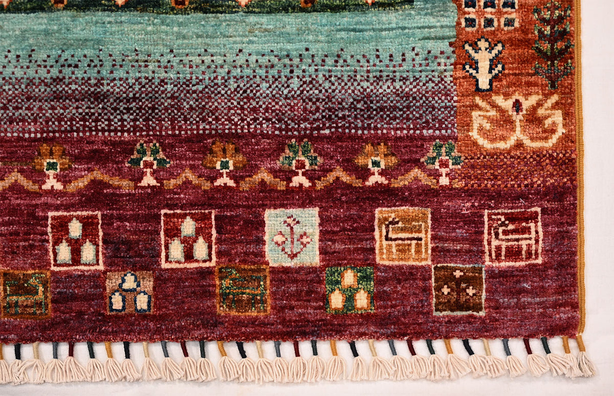The corner of a handmade Afghan Loribaft Gabbeh rug with multicolour geometric motifs and off-white fringe trim at edge