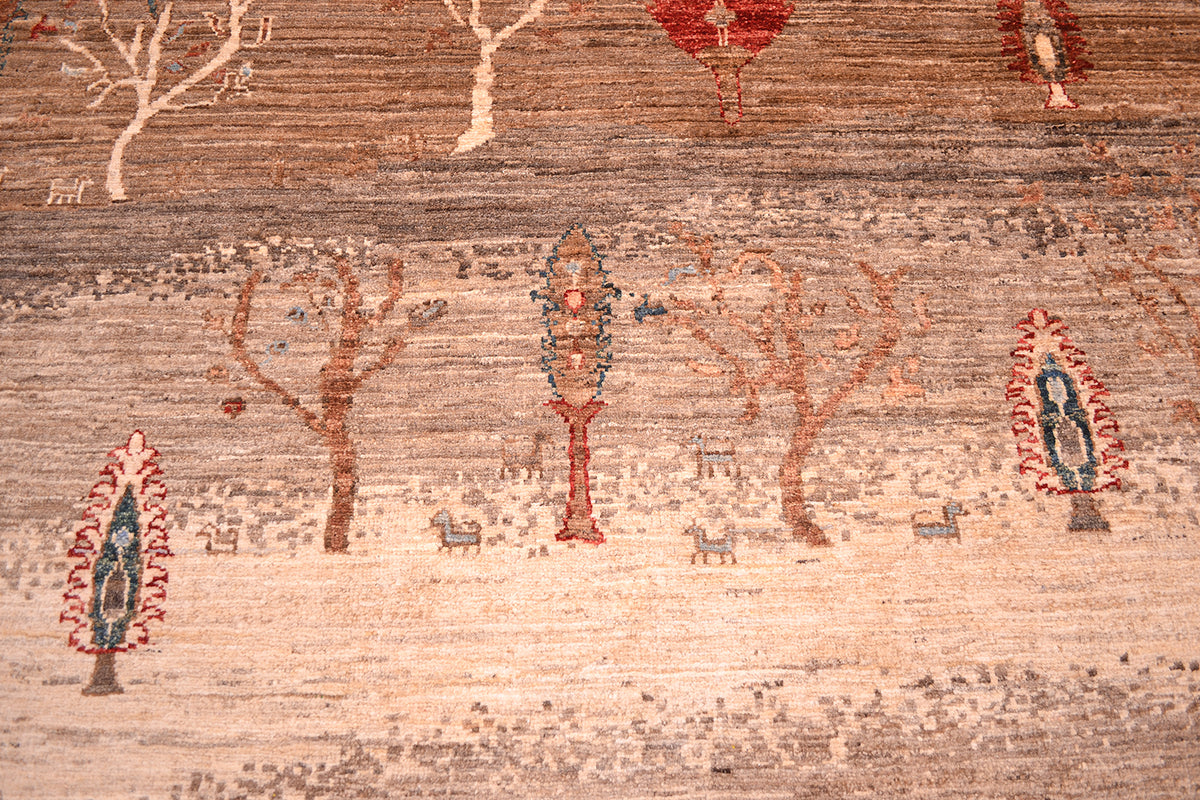 Close-up of a handwoven Afghan carpet showing a stylised landscape scene with trees, small animals, and a central figure in muted earth tones and red accents.
