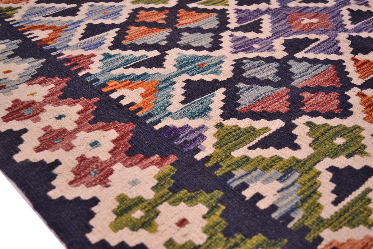 A close-up of a Afghan woven colourful kilim rug showing its detailed geometric and floral patterns in navy, beige, green, orange, and purple.