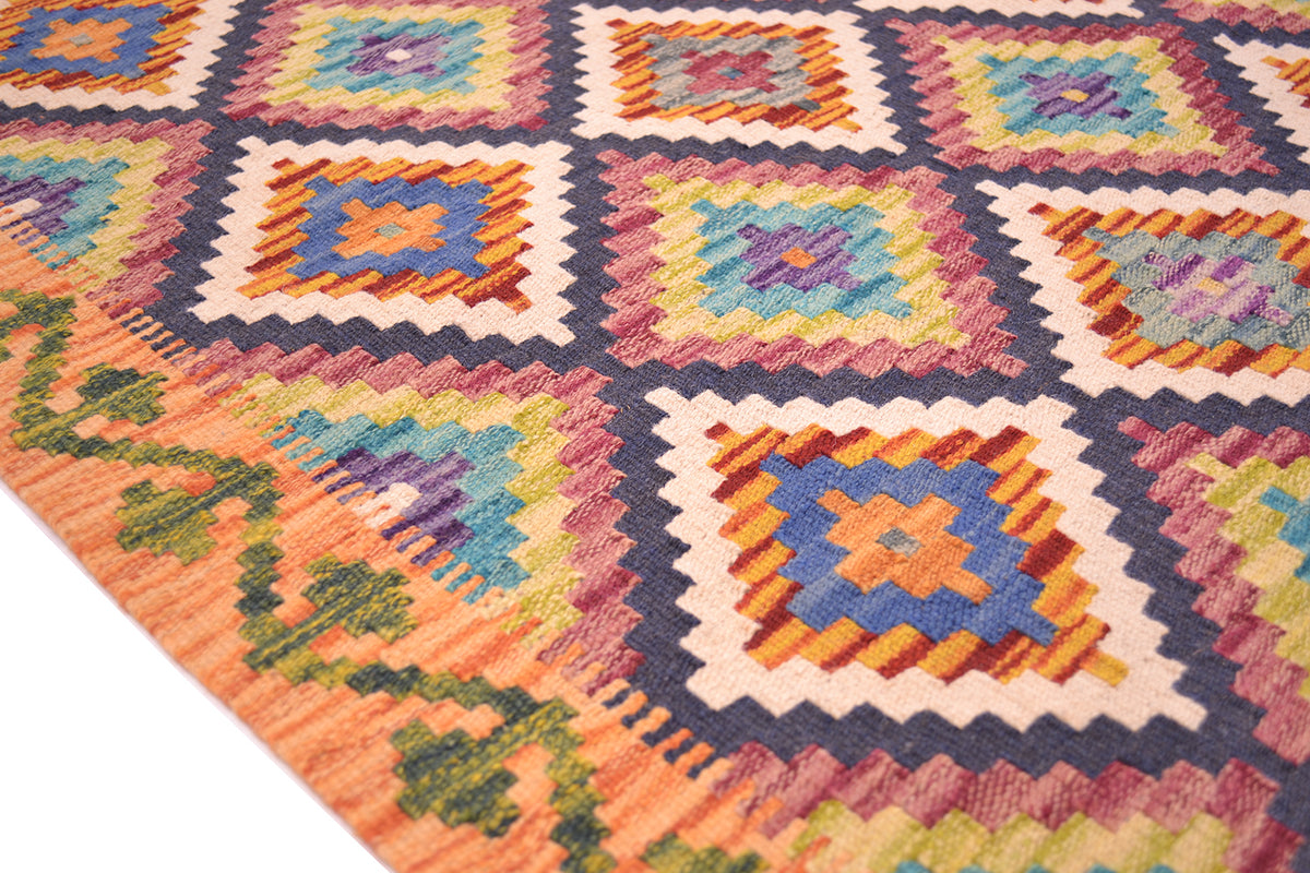 A close-up of a colourful handwoven multicolour Kilim short runner rug with a geometric diamond pattern in orange, blue, yellow, green, and purple on a white background.