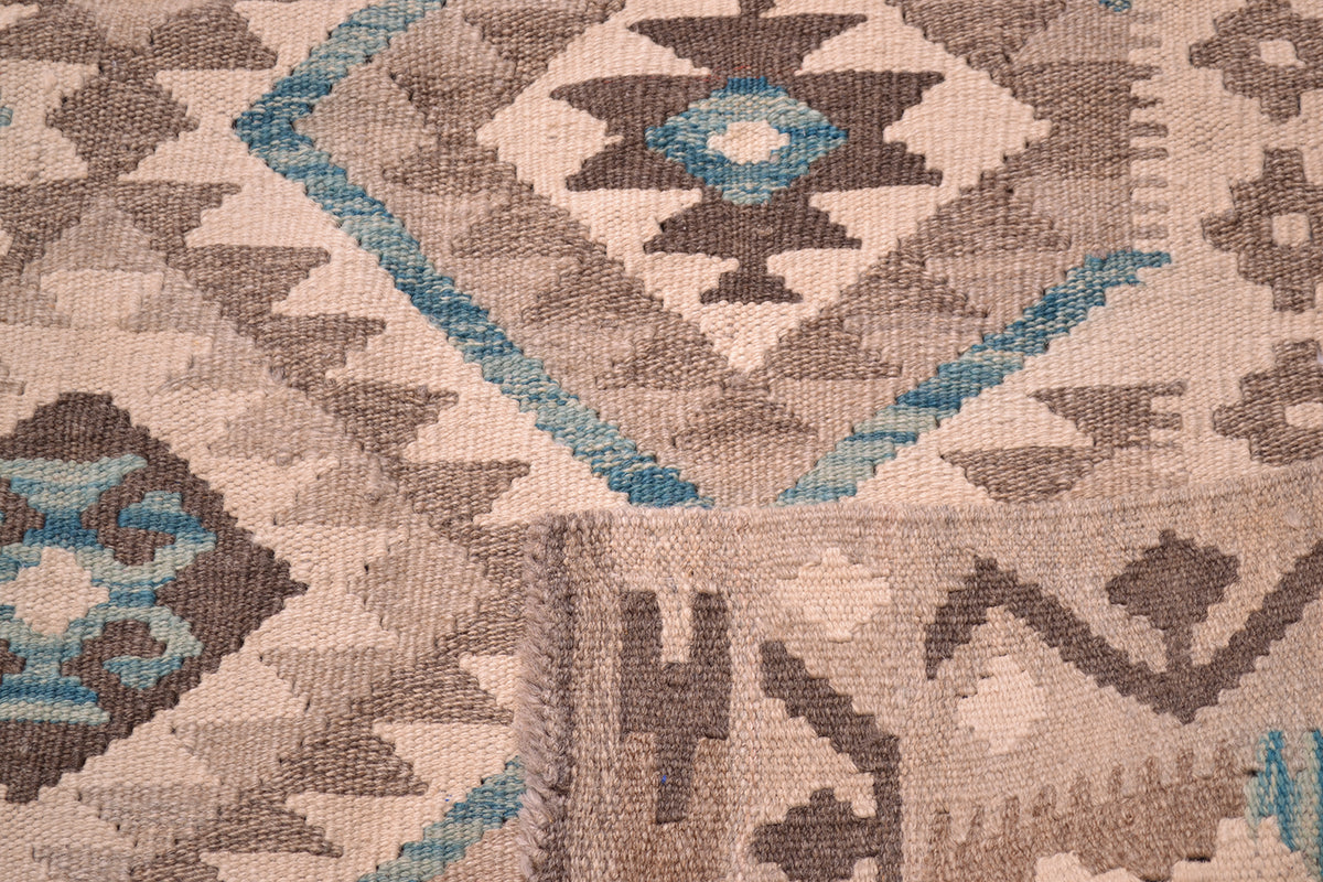Close-up of a woven Afghan rug with a geometric tribal klilim pattern in beige, brown, grey, and teal.