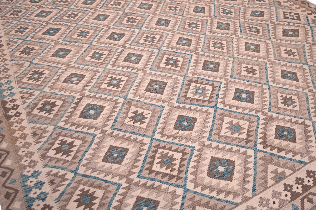 A close-up view of a handwoven large Afghan Kilim rug with a repeating geometric pattern in beige, brown, grey, and teal.