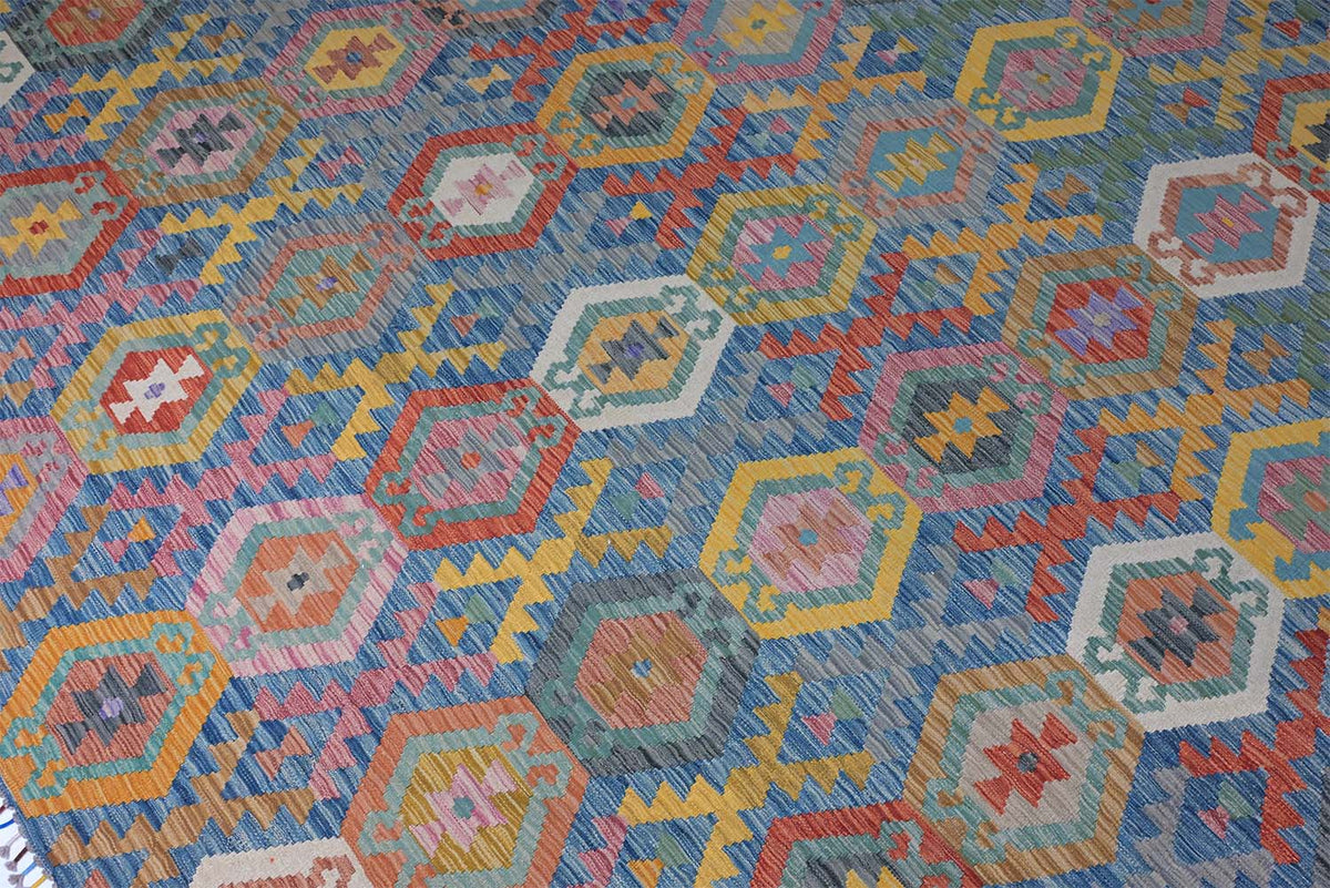 A close-up of a Giant Handwoven Afghan Kilim rug with a colourful geometric pattern featuring hexagons and stars in blue, pink, yellow, orange, and white.