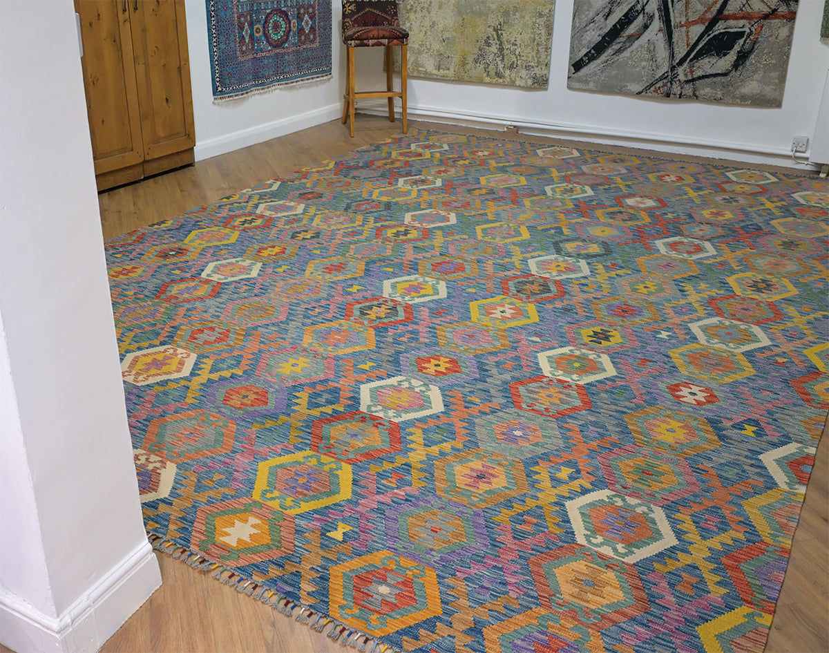 A Giant Handwoven Afghan Kilim rug with a colourful geometric pattern, shown in a room with wooden floors and other wall hangings.