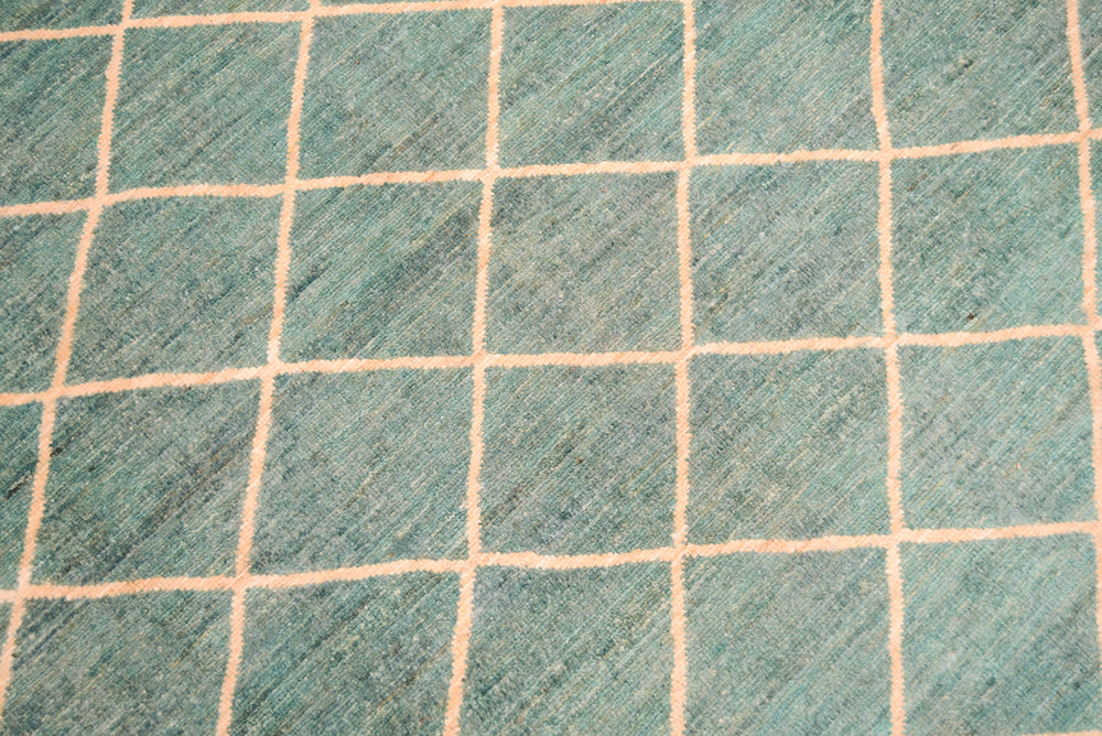 Close up detail of main field and lattice geometric pattern of handmade afghan carpet in light topaz turquoise and cream tonalities. Pure wool pile.