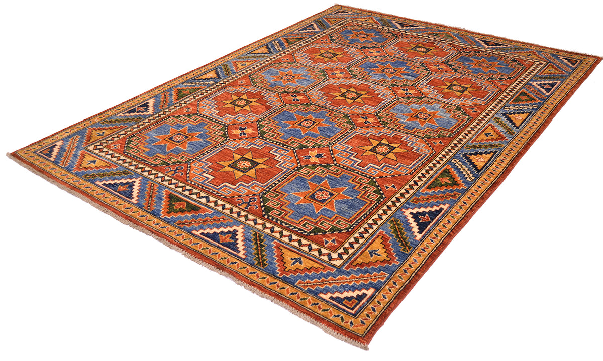Angled view of handknotted colourful carpet with rust red, mid to dark blues, greens, golden ochres light golden creams that highlight geometric devices and inner borders. Rust red field with memling guls and blue background of geometric border. Shown on a white background.