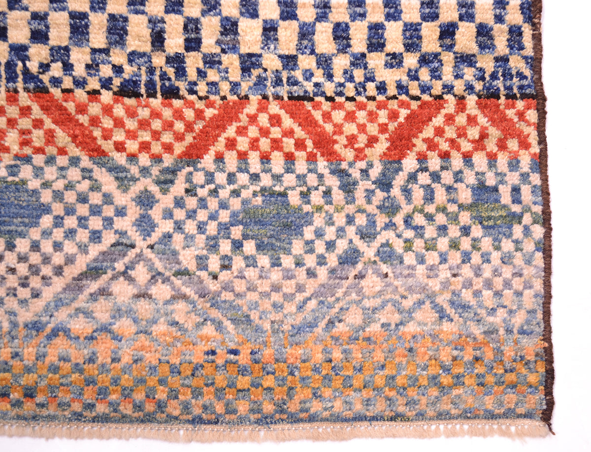 Corner detail of Handknotted carpet wirh cream and blue geometric patterning. Fringe showing pure wool warps.