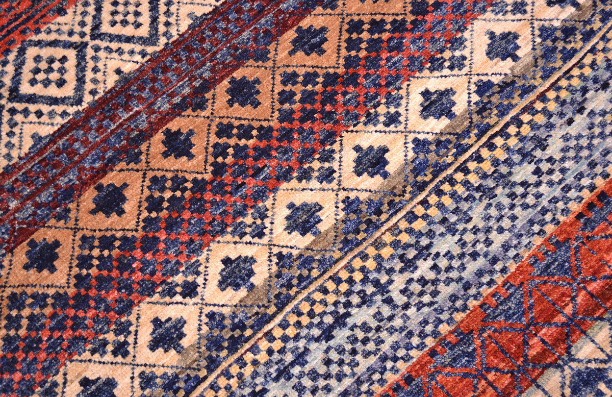 Close up detail of main field of handknotted carpet from Afghanistan in multiple colours of banded patternig. Motifs in a deep rich blue.