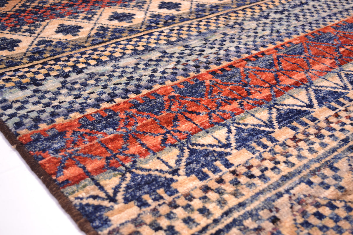 Closeup of edge of modern geometruc Afghan carpet with oure wool pile woven on wool warps. Banded striped of ground colours with blue geometric patterning.