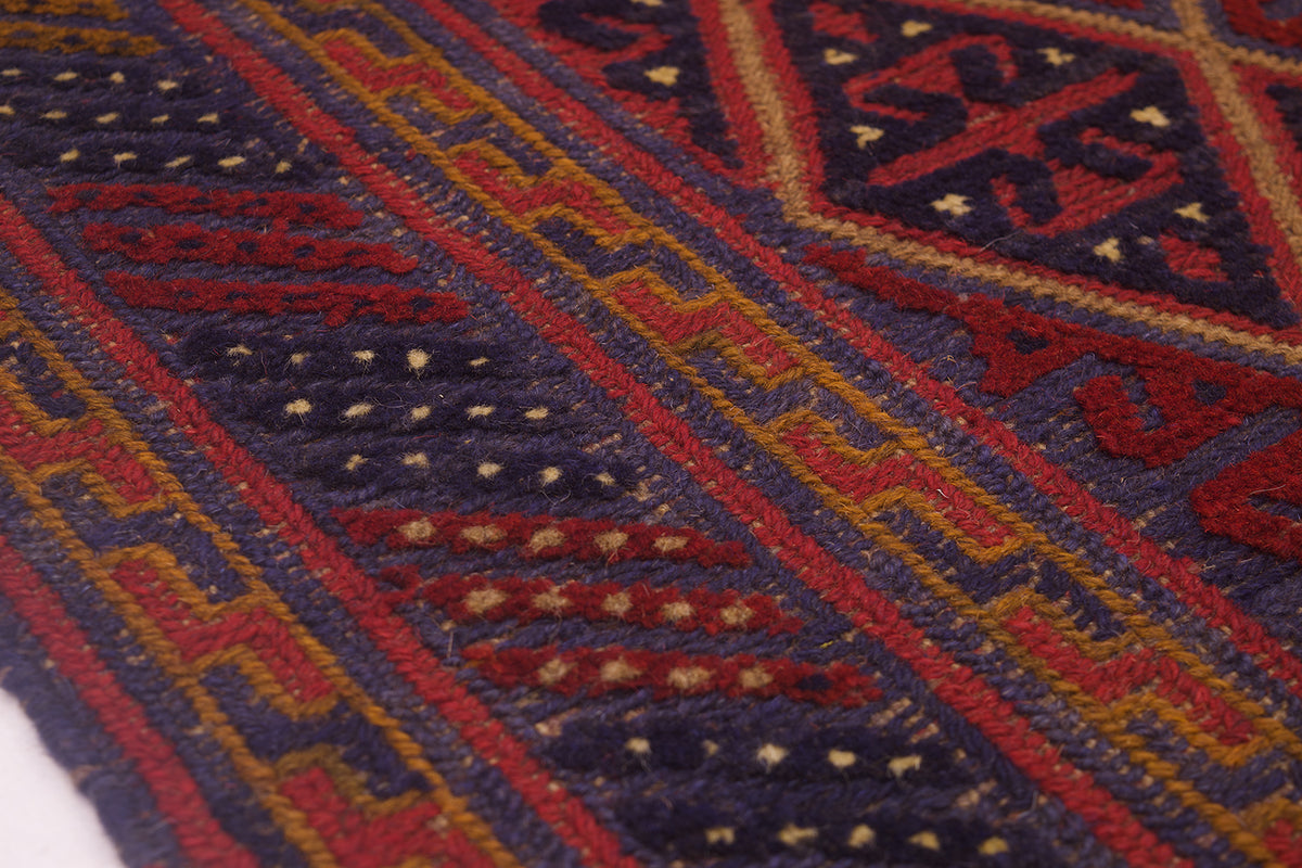 Close-up of a woven Afghan Mushwani square rug with geometric patterns in dark navy blue, red, ochre yellow, and cream.
