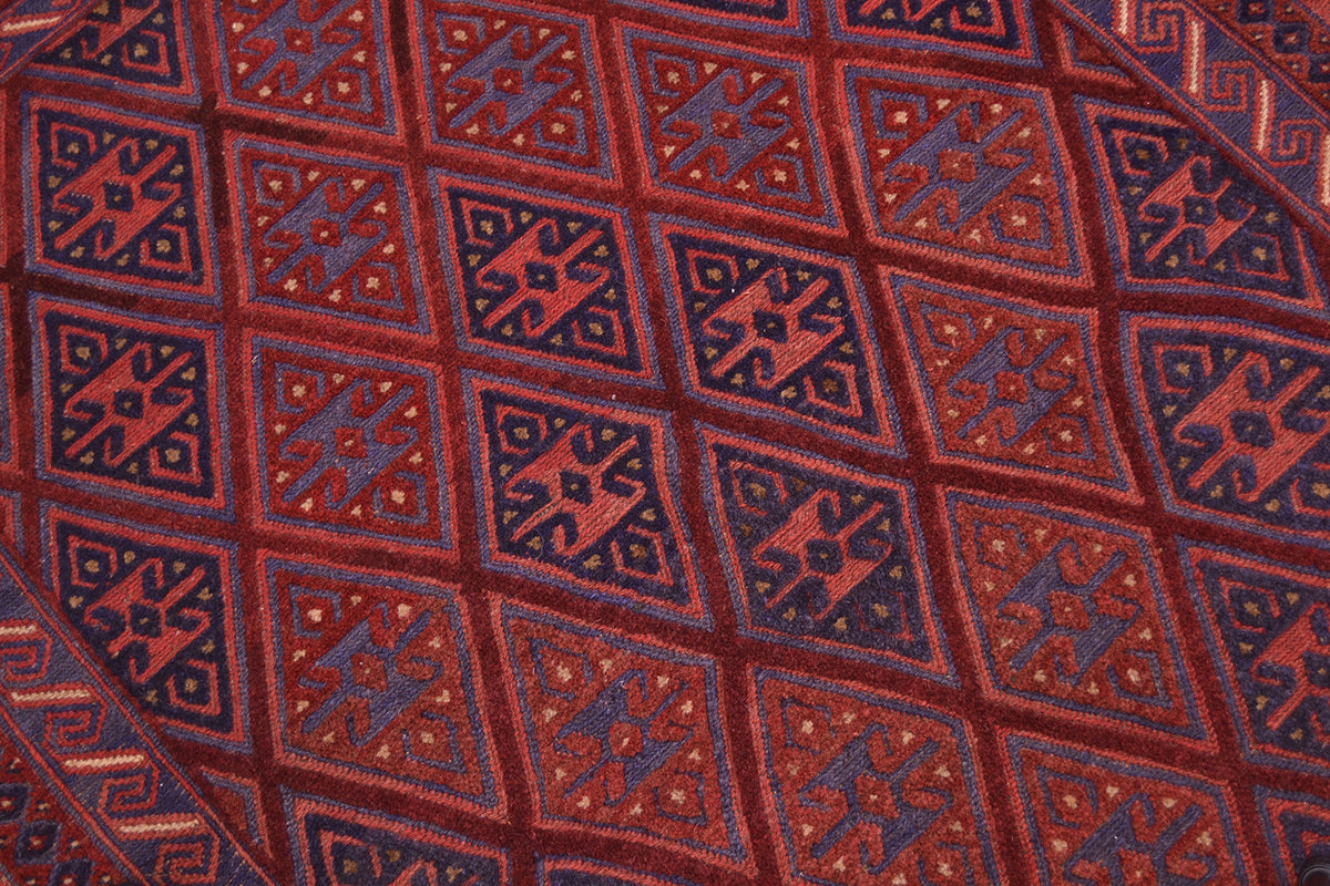 A close-up of a handwoven wool Afghan Mushwani rug with a repeating diamond pattern in dark red, rust, and deep navy blue.