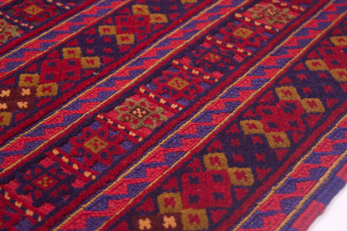 A close-up of the border of a fine mushwani carper with bold geometric stripes in red, blue, brown, and olive green, showing detailed pile texture.