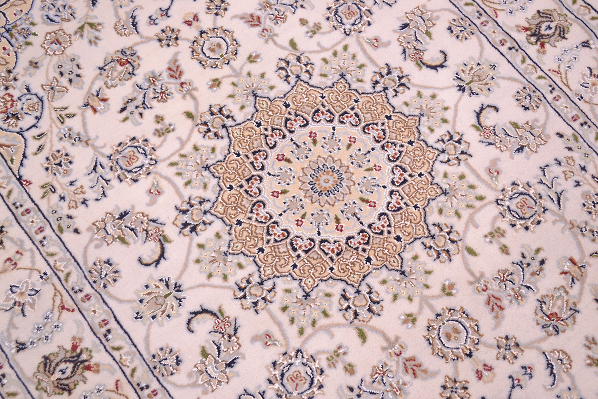 A close-up of an ornate Persian-style Indian Nain area rug with a central floral medallion and intricate scrolling motifs in beige, navy blue, and muted green on a pale cream background.