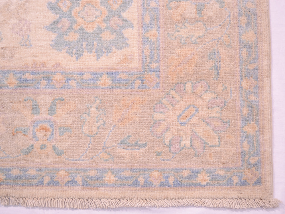 Corner detail of handmade rug with cotton warps and soft coloured field and border
