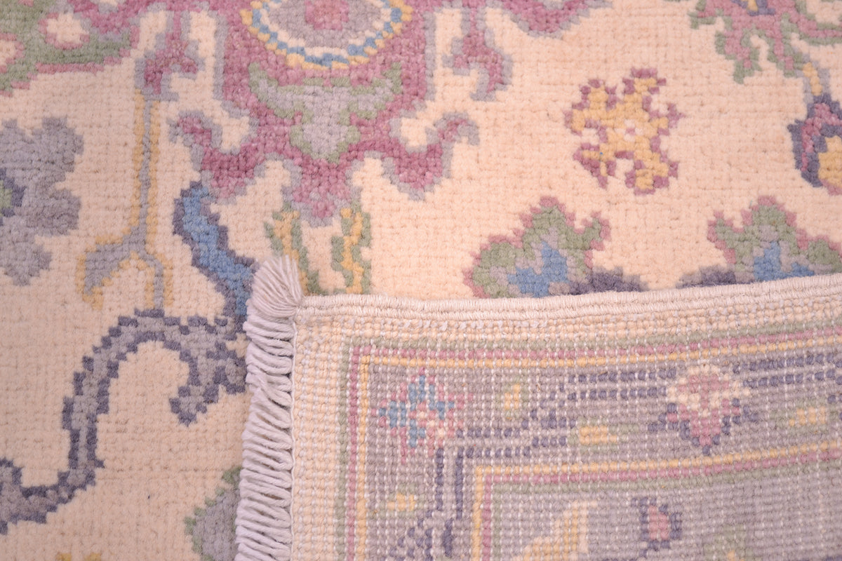Handmade Oushak rug with fringed edge; multicolor floral pattern on cream field.
