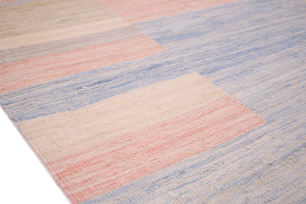 Close up detail of striped blocks of tone of kilim woven by hand with coral pinks and blues and cream tones.