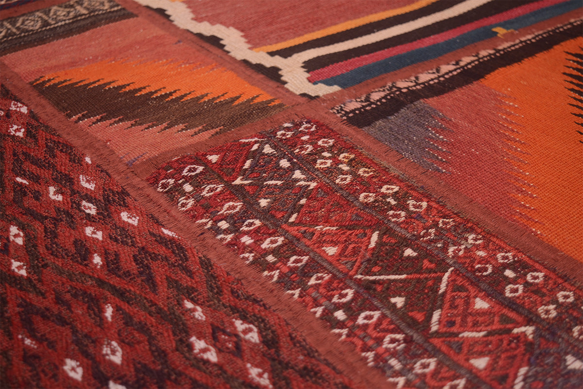 Close-up of a woven kilim patchwork rug with geometric and tribal-inspired patterns in rust red, orange, brown, black, and small white accents.