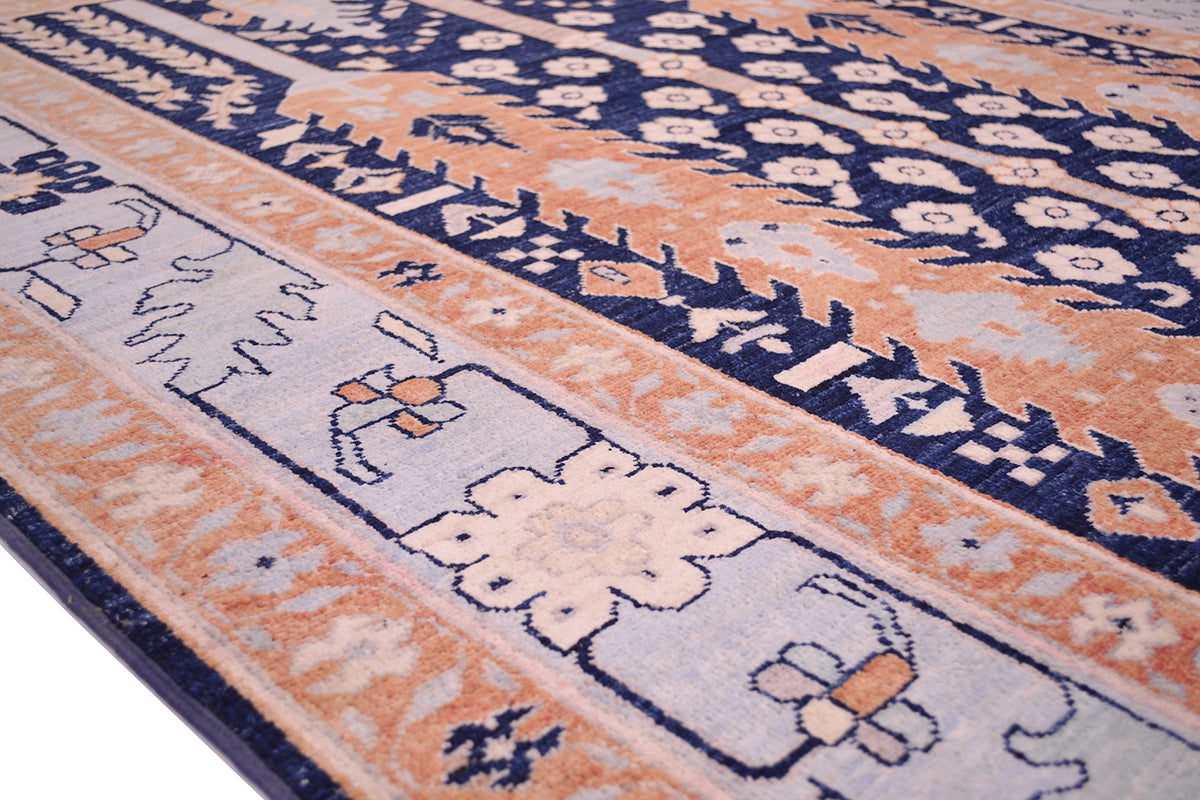 A close-up of a patterned Afghan pictiorial area rug with a traditional design, featuring bands of navy blue, peach, cream, and light blue.
