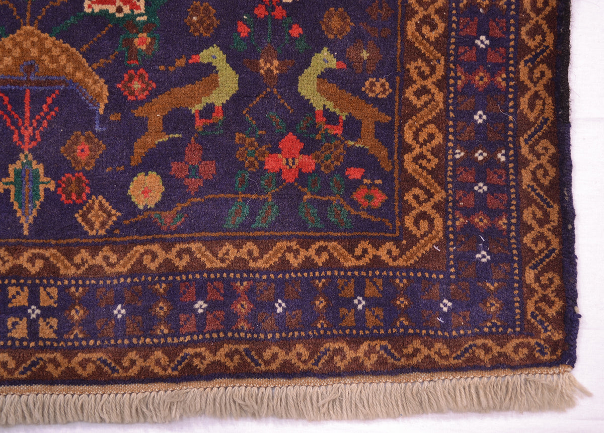 Close-up of a traditional patterned rug corner showing a dark navy blue field with two birds, floral motifs, and ornate brown and beige borders with fringe.