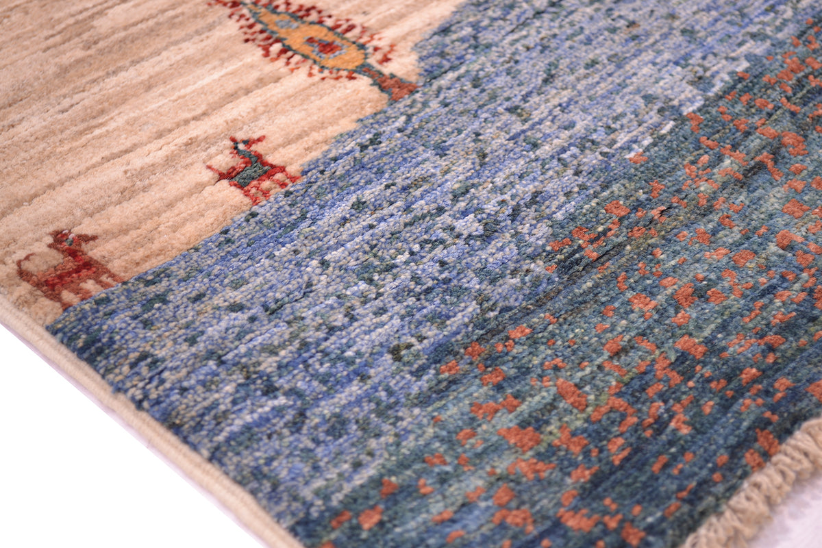Close-up of a handwoven Afghan Loriabft pictorial rug showing a beige and blue patterned design with small red and orange decorative motifs.