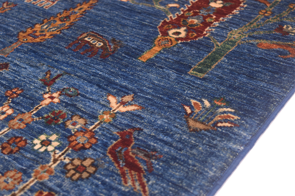 A close-up of a blue patterned Afghan pictorial rug with traditional motifs including birds, floral elements, and abstract shapes in rust, beige, green, and cream.