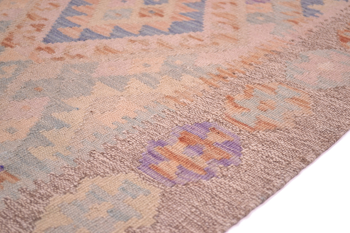 Close-up of a woven a soft colour Afghan Kilim runner showing a textured pattern in dusty pink, beige, light blue, and lavender purple.