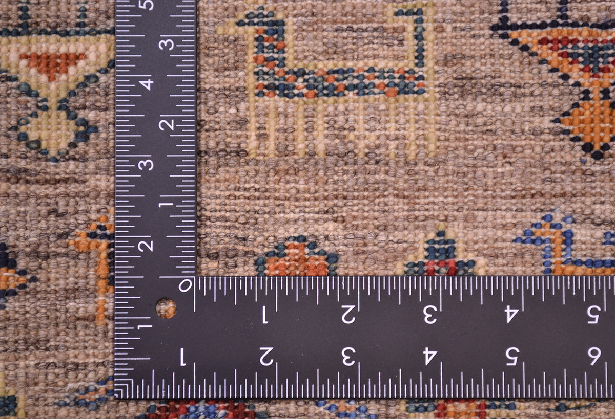 Close-up of the hand-knotted weave of a patterned fine Afghan Samarkand rug with a dark L-shaped metal ruler placed along the corner to show the quality and density of the knotting.