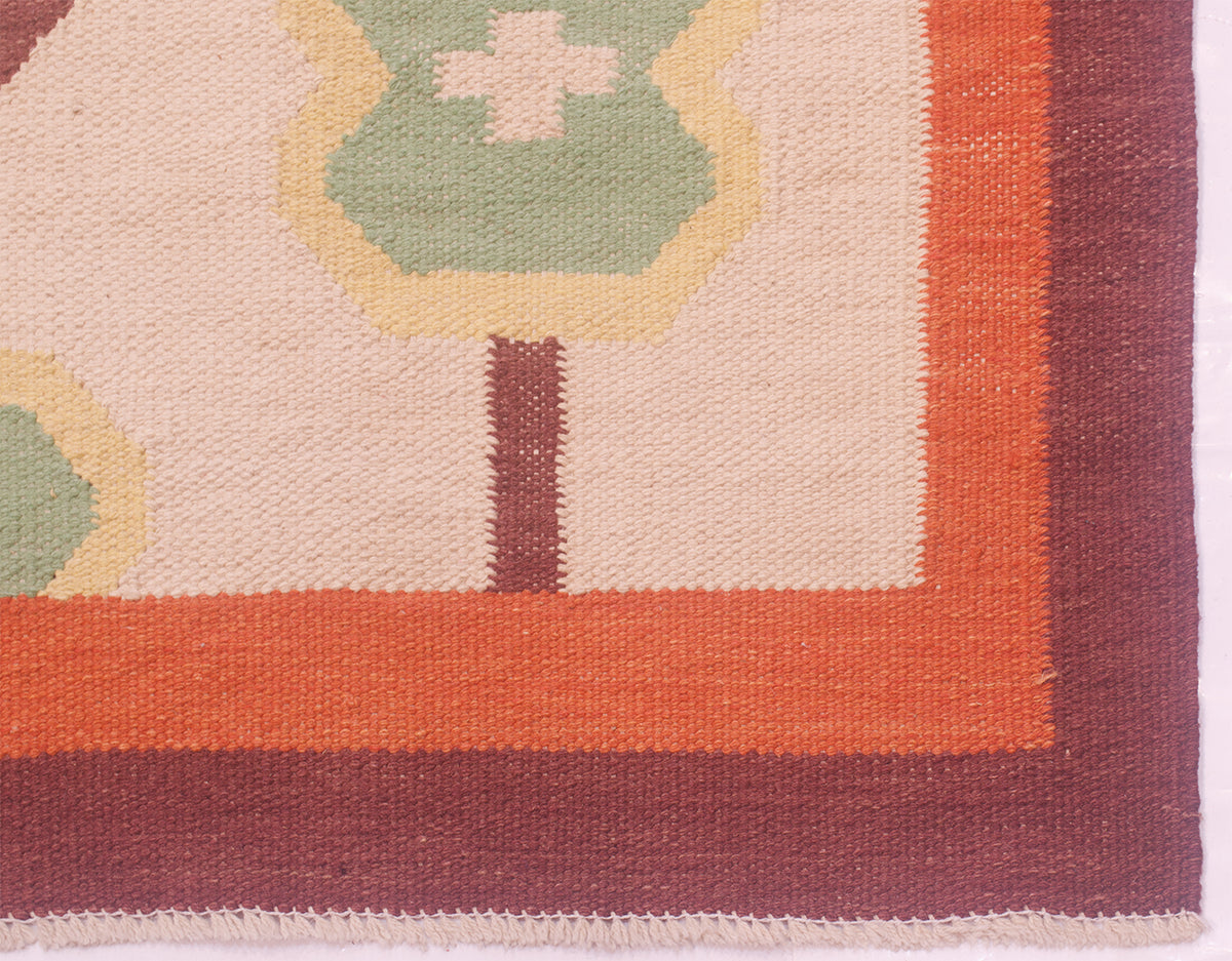Close-up of an Afghan woven Scandi Kilim rug corner showing a cream field, orange border, dark brown border, and green and yellow geometric motifs.