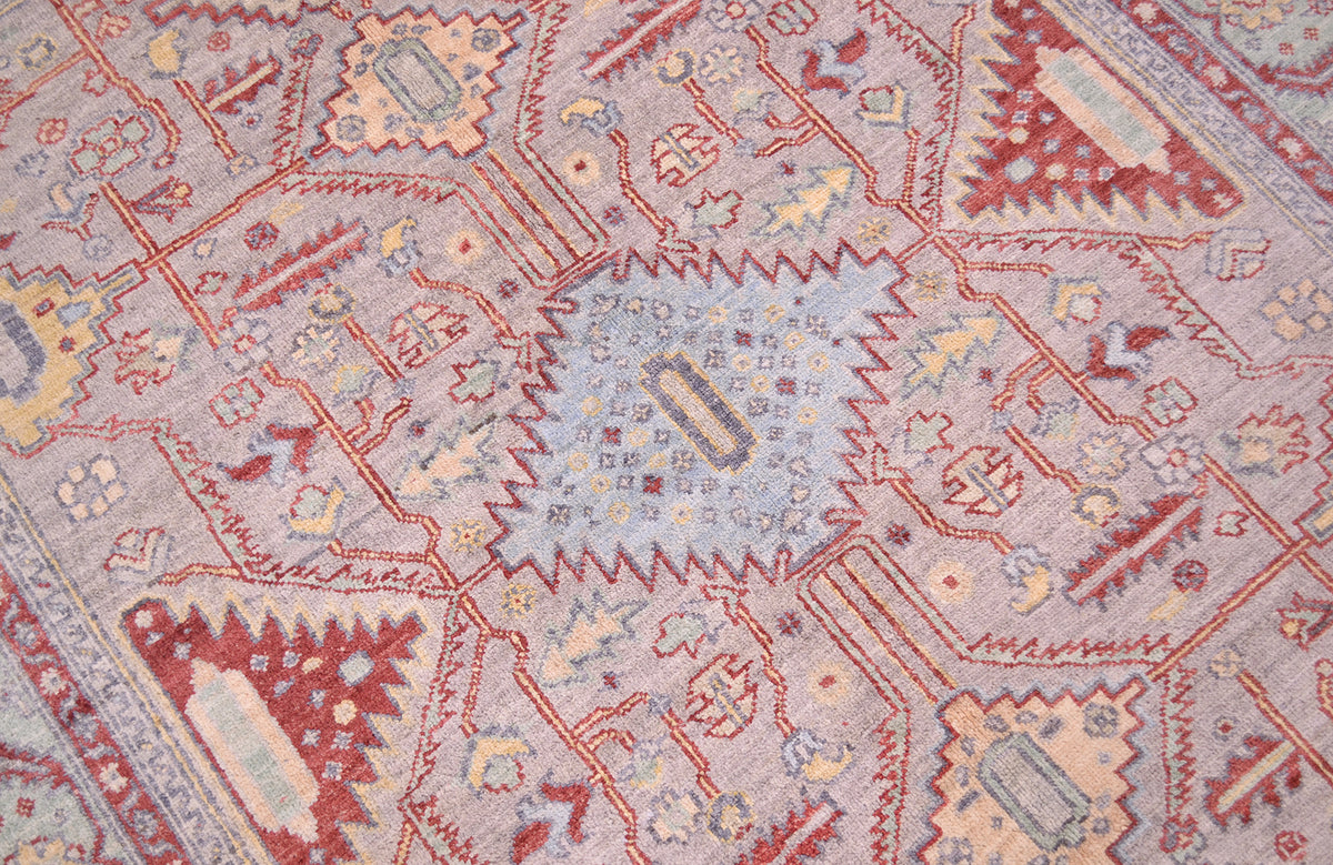 Close up detail of handknotted rug with geometric vine and florettes and appendages radiating out from several serrated diamond medallions. Soft silver grey main field hue with accents of light golden yellow.