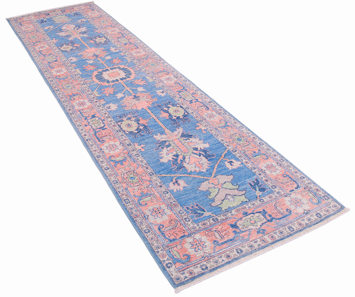 Angled view of Serapi design hand knotted runner with blue field and pinks and green accents. Hightlights of white/cream and woven on a cotton foundation.